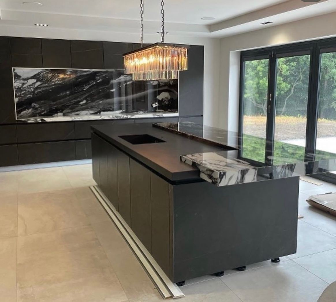 Modern kitchen with marble island, black cabinetry, and a glass chandelier.